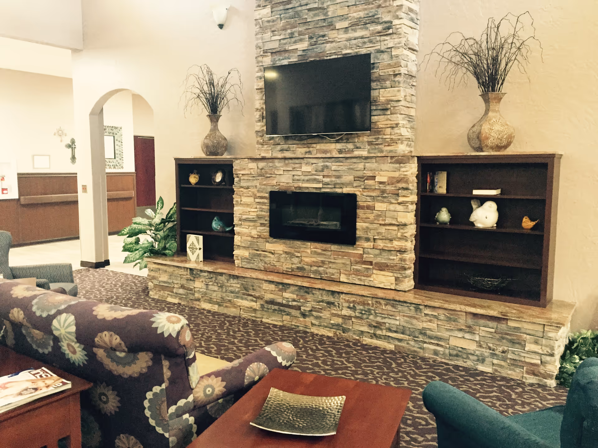 Cozy sitting area with patterned sofas facing a stone fireplace wall with a mounted TV and built-in shelves.