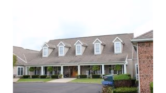 Front exterior of a single-story assisted living building with a covered porch, dormer windows, and landscaped lawn.