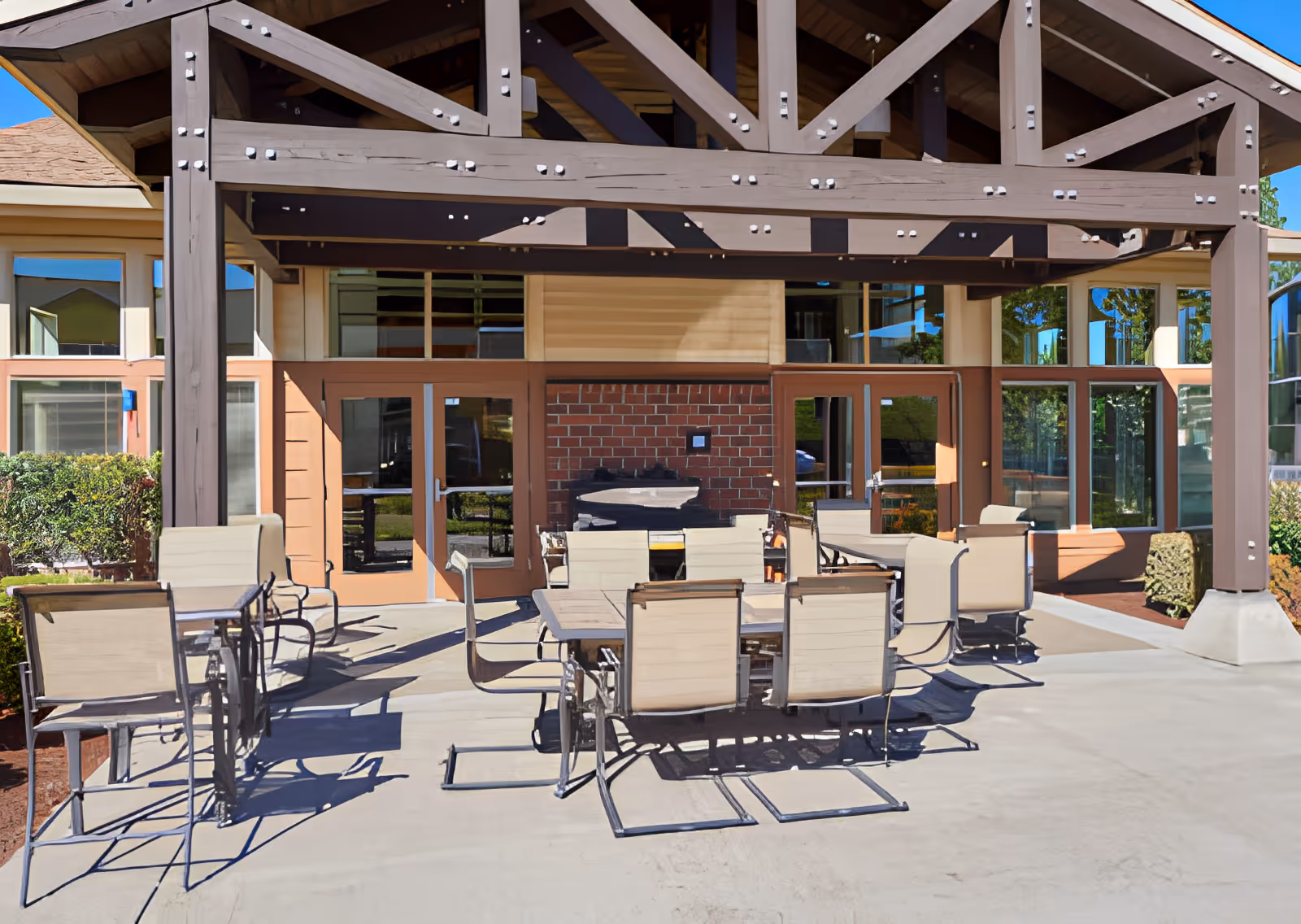 Outdoor patio area at Elliott Residence with multiple tables and chairs arranged under a wooden pergola structure, adjacent to a building with large windows and double glass doors.