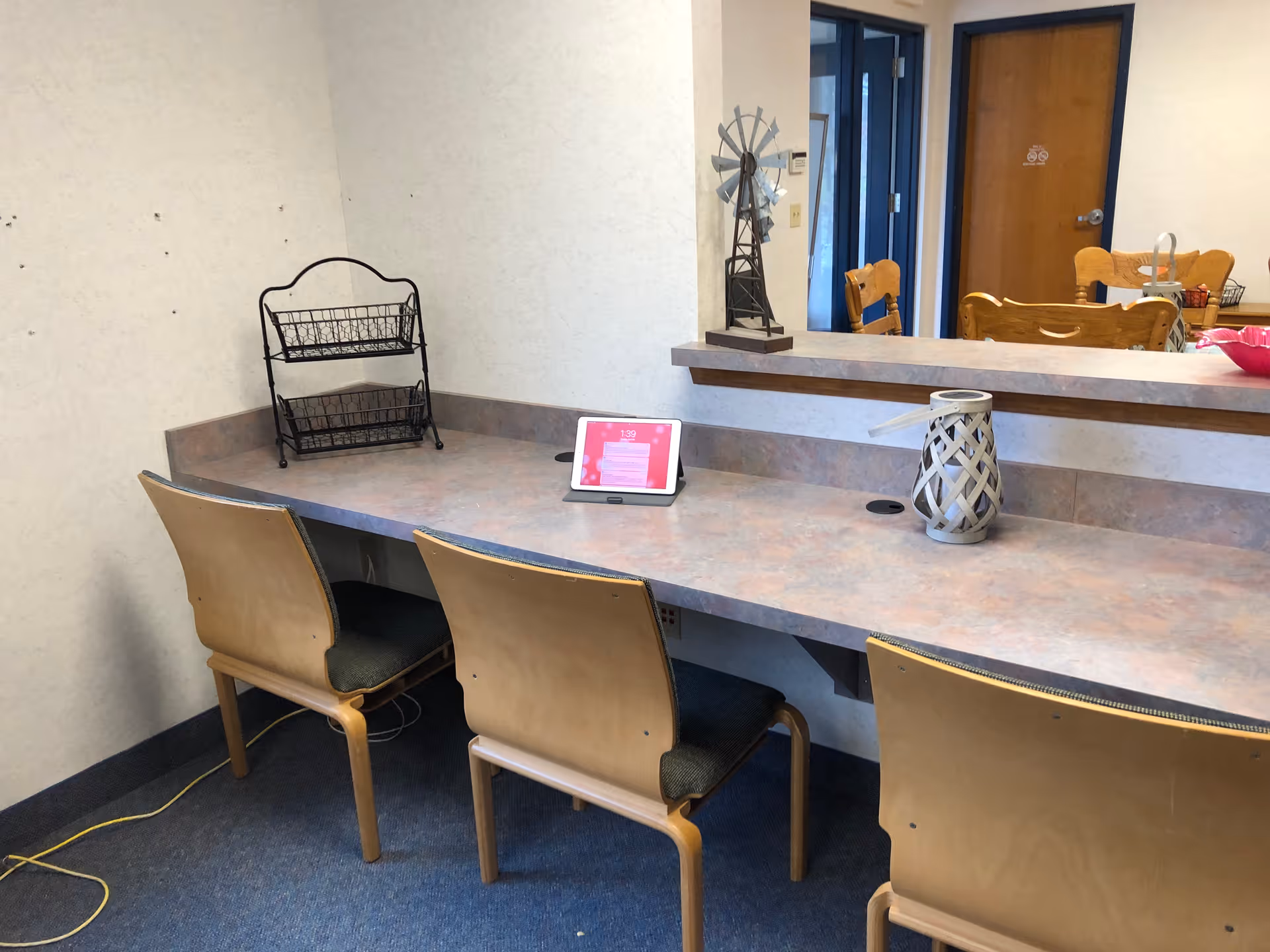 Long countertop workspace with three wooden chairs, a tablet and decorative items in a communal senior living area.