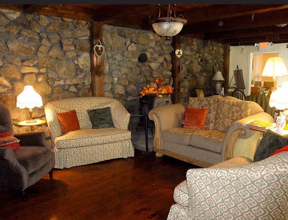 Cozy living room with upholstered sofas and armchairs, table lamps, and a stone wall background.