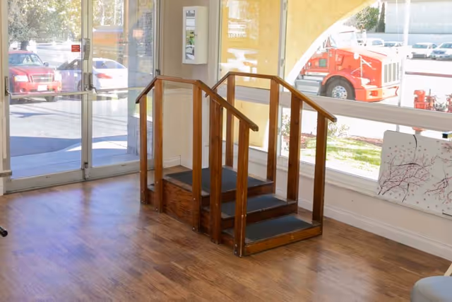 Small wooden practice stairs in a bright entry room with large windows and glass doors showing parked cars outside.