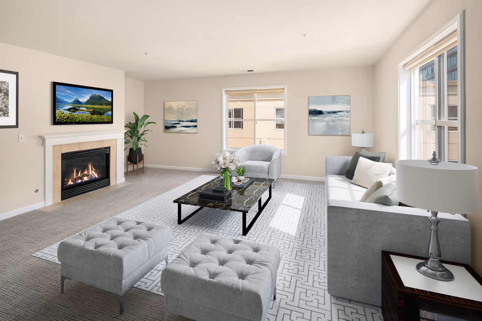 A bright and modern living room with a fireplace, a wall-mounted TV above it, a large window letting in natural light, a gray sofa with cushions, two gray tufted ottomans, a gray armchair, a black marble coffee table with decorative items, a patterned area rug, two table lamps, and framed artwork on the walls.