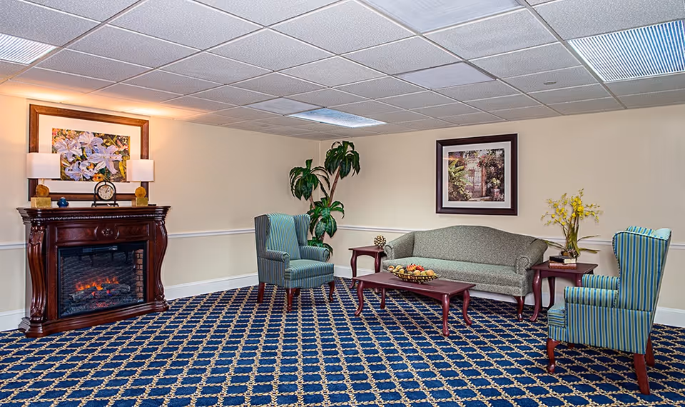 Carpeted common sitting room with a sofa, striped armchairs, a coffee table, decorative fireplace and framed artwork.