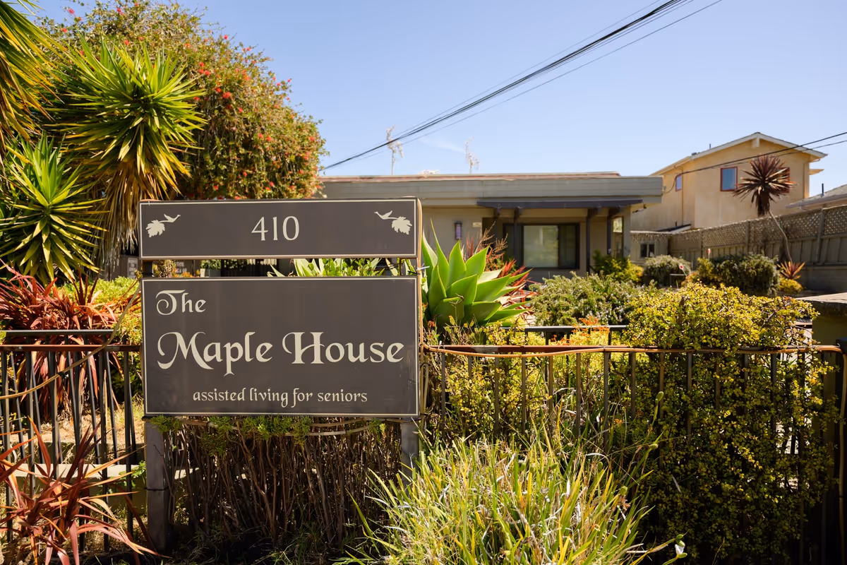 Exterior view of The Maple House senior living facility with its sign and landscaped front yard.