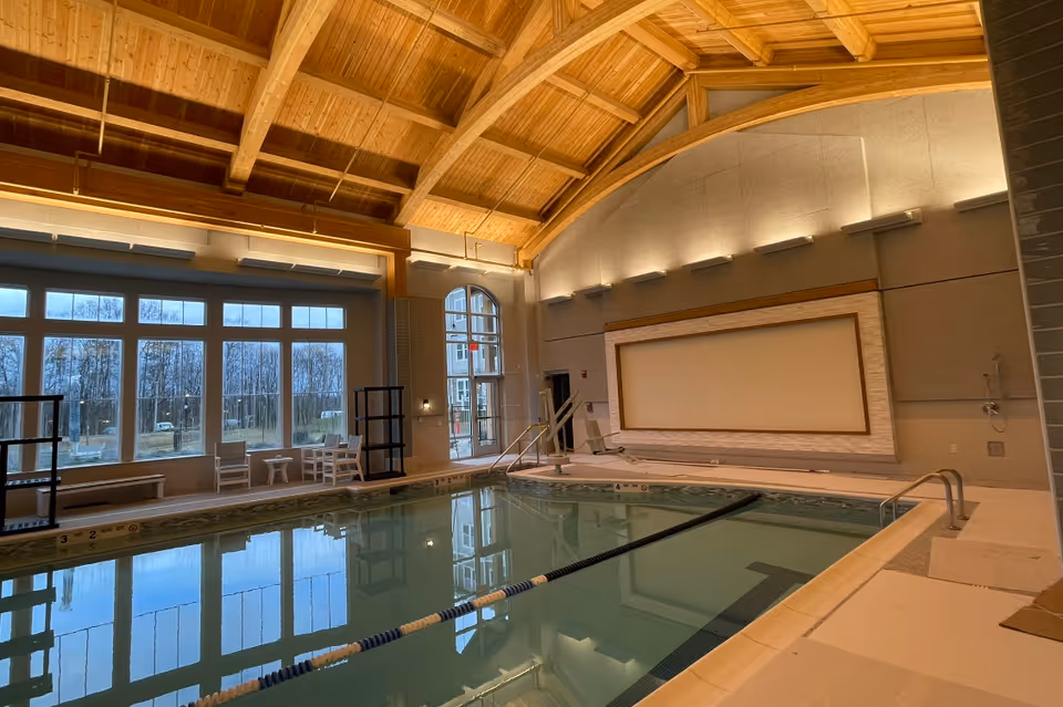 Indoor swimming pool with a lane divider, seating by large windows, and a high wood-beamed ceiling.