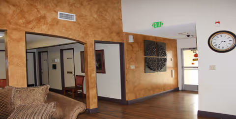 Interior common area with brown textured walls, a sofa, clock, and a green exit sign.