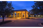 Warmly lit building entrance with columns and curved driveway at dusk.