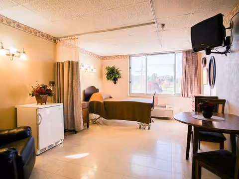 Interior nursing facility room with bed, privacy curtain, and mounted TV.