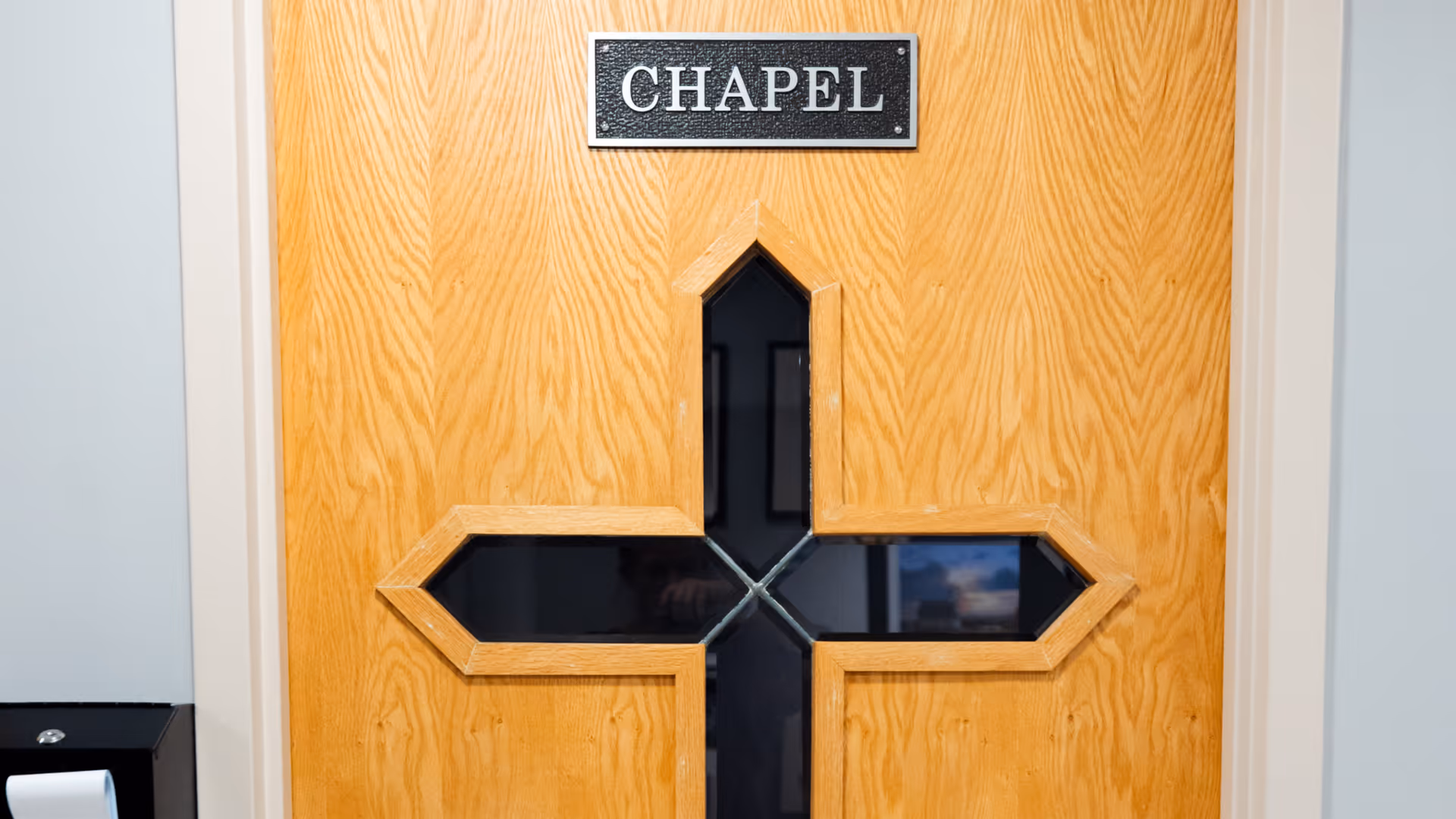 A wooden door with a cross-shaped window in the center and a black sign above it that reads 'CHAPEL'.
