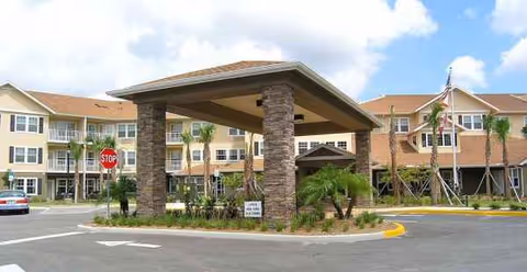 Exterior view of a senior living facility entrance with a stone porte-cochere and landscaping.
