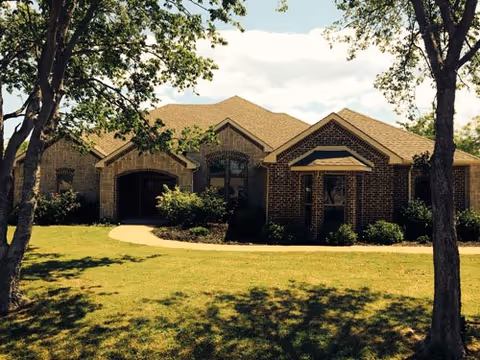 Exterior view of a single-story brick building with a gabled roof, surrounded by trees and a well-maintained lawn under a partly cloudy sky.