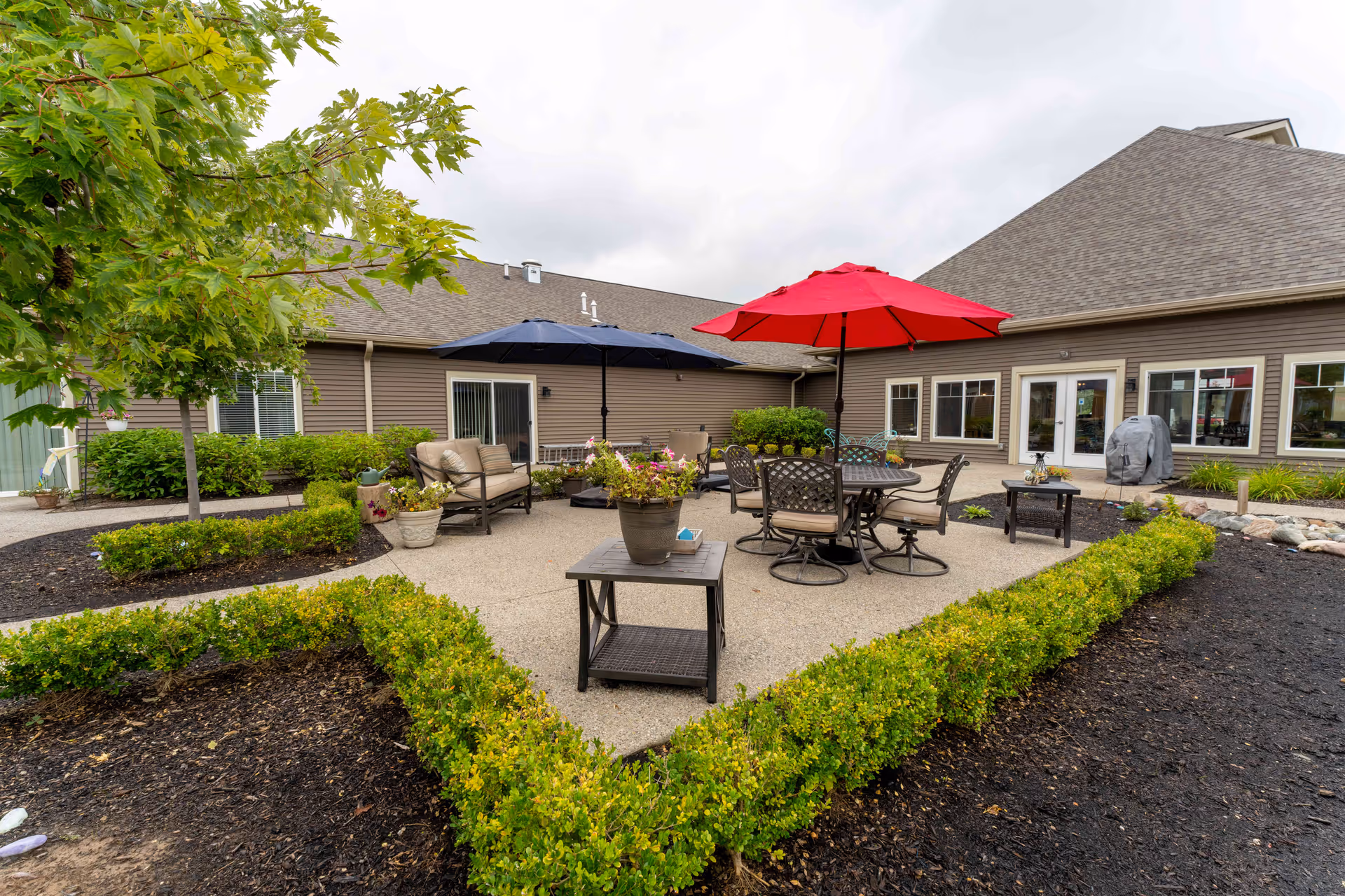Outdoor courtyard patio with seating, tables, umbrellas, and landscaping outside a senior living facility.