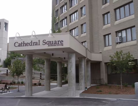 Entrance canopy reading 'Cathedral Square Senior Living' supported by concrete columns in front of a multi-story building.