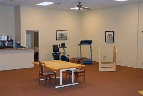 A spacious rehab facility common area with a table, chairs, and exercise equipment.