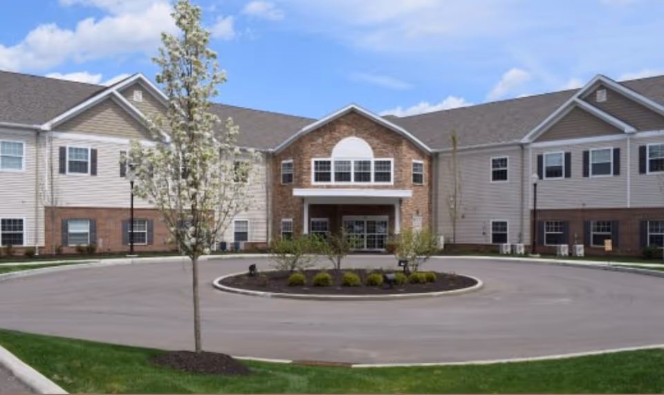 Front exterior of a two-story senior living building with a covered main entrance, circular driveway, and landscaped island.