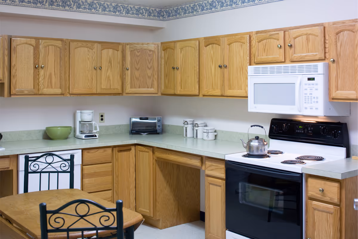 Small kitchen with oak cabinets, countertop appliances, a microwave and electric stove, and a table with chairs.