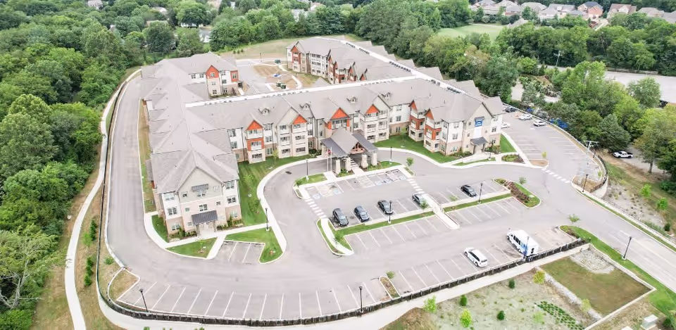 Aerial view of a large senior living facility named Harmony At Bellevue, showing a multi-wing building surrounded by parking lots, trees, and greenery.