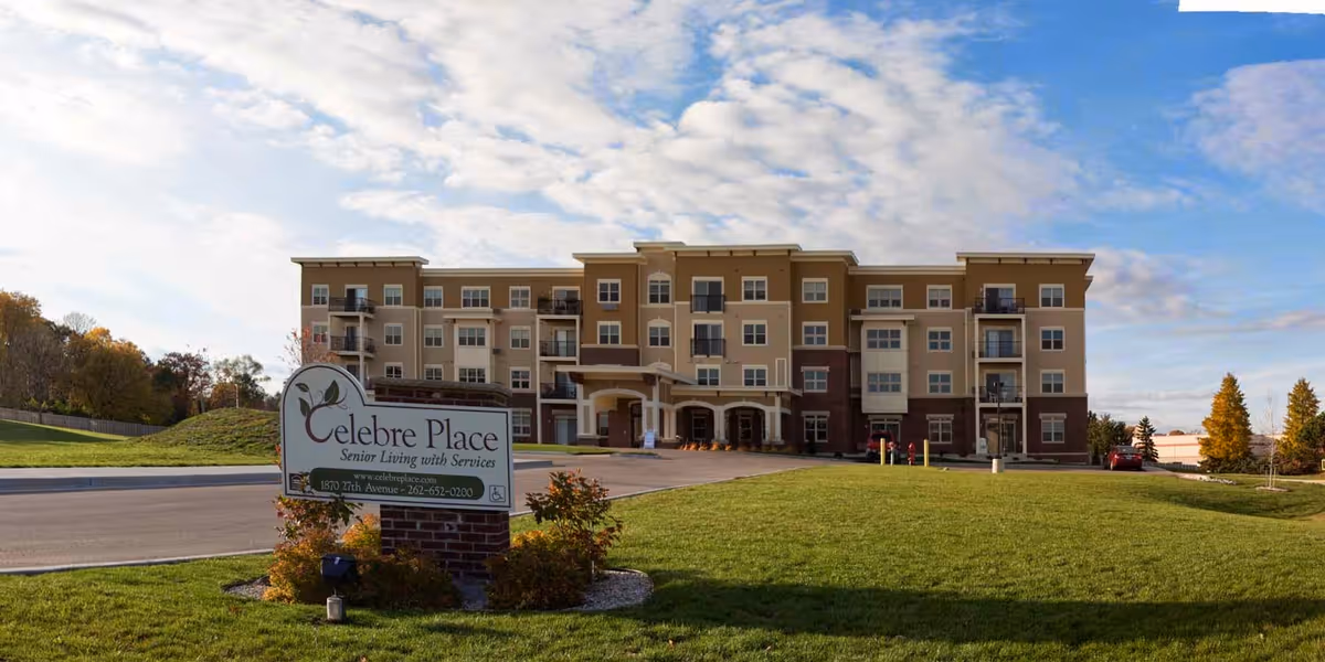 Exterior view of Celebre Place, a multi-story senior living facility with balconies, a driveway, and a well-maintained lawn under a partly cloudy sky.
