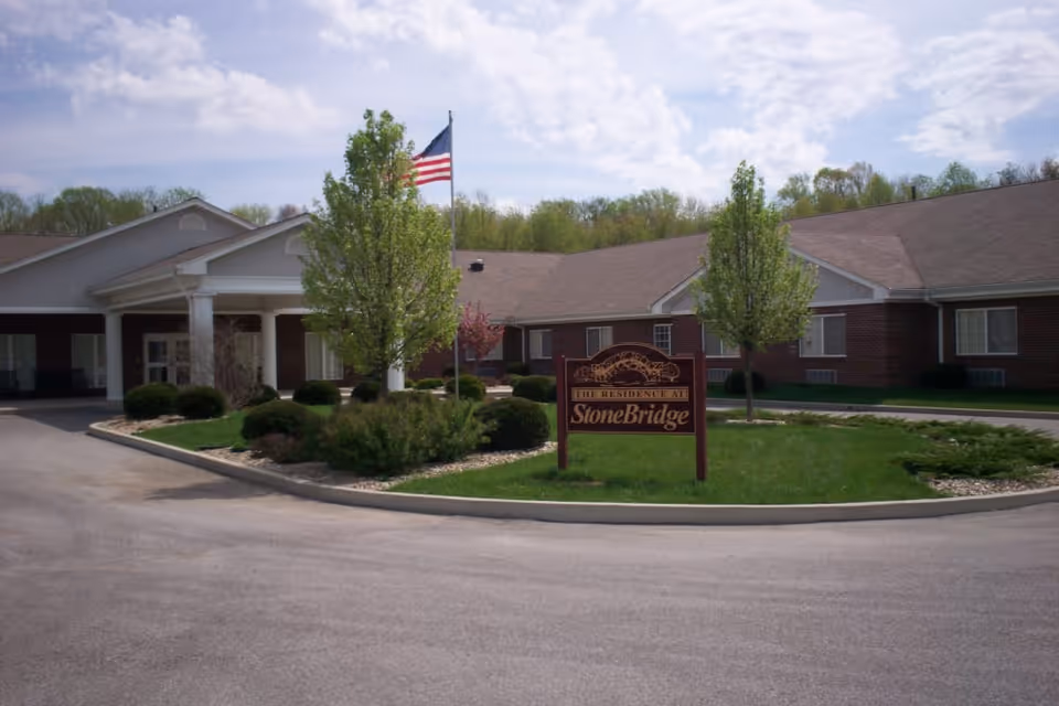 Front exterior of the StoneBridge Health Campus building with a landscaped circular driveway, an American flag, and a sign reading 'StoneBridge'.