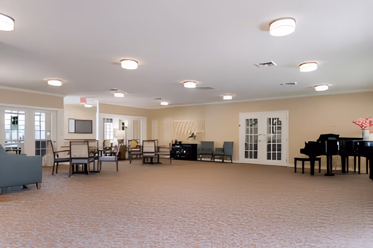 Spacious common lounge with chairs, tables and a grand piano in a well-lit room.