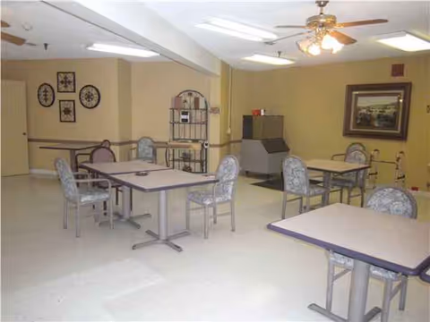 A bright dining room with multiple square tables and patterned chairs in a senior living center.