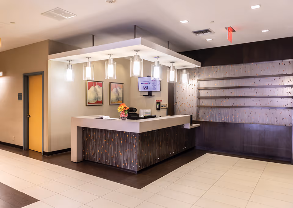 Modern assisted living reception desk and lobby with pendant lights, artwork, and empty shelving.