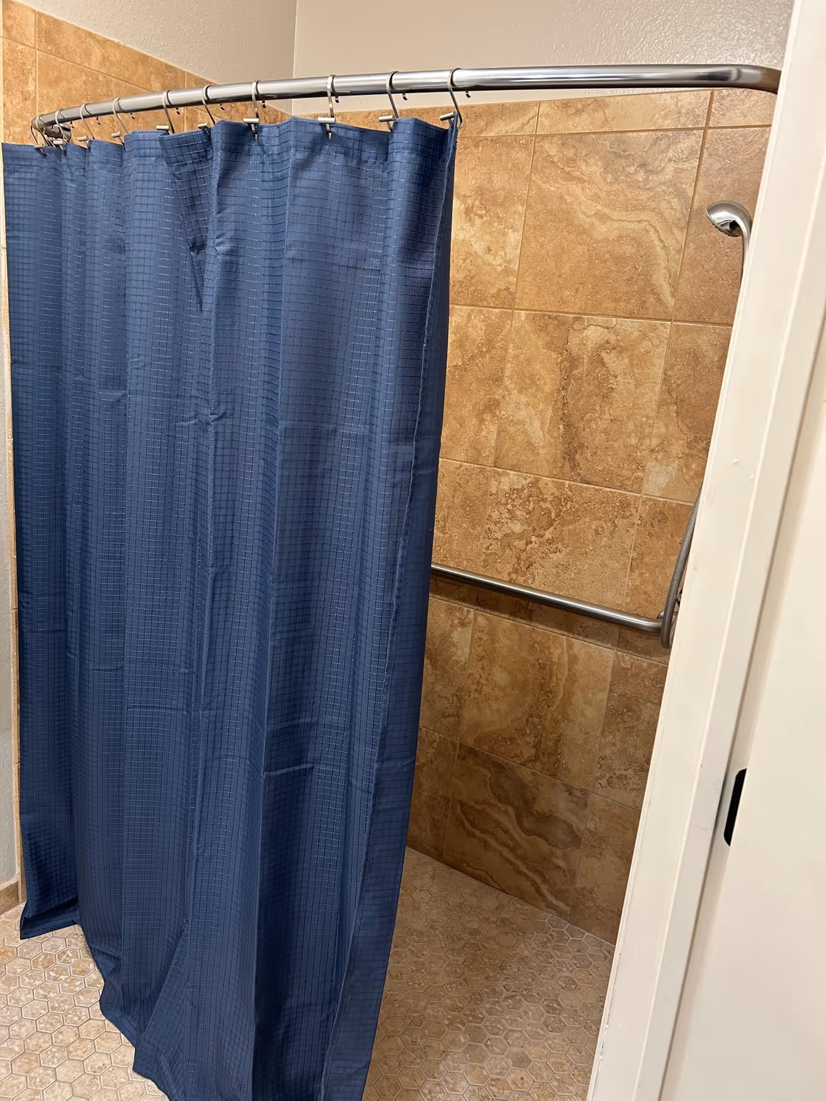 Shower stall with a blue curtain, tile walls, a grab bar and a curved shower rod.