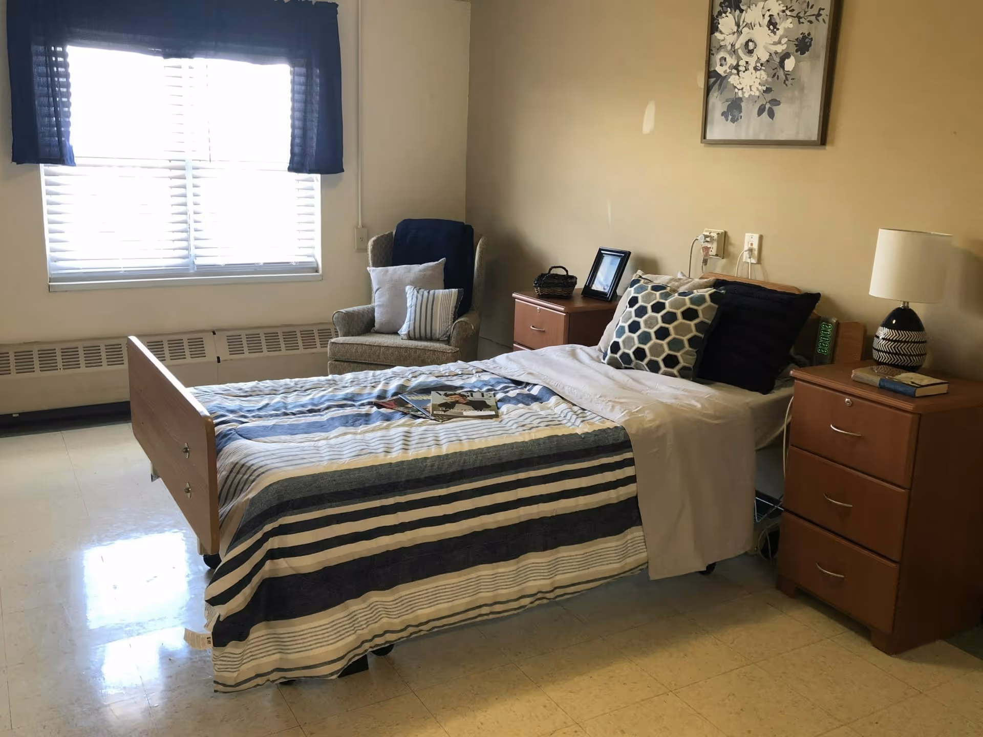 Single-occupancy bedroom with a striped bed, two nightstands, an armchair and a window with blinds