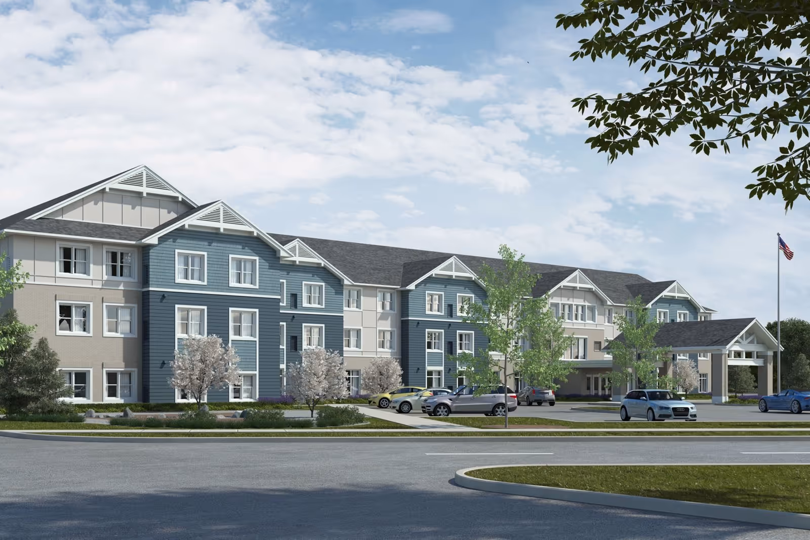 Three-story senior living facility building with blue and beige siding, landscaped grounds, a parking lot, and an American flag.