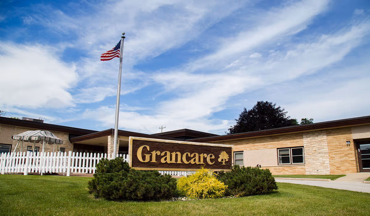 Front view of Grancare Gardens Assisted Living with sign, flag, and landscaping.