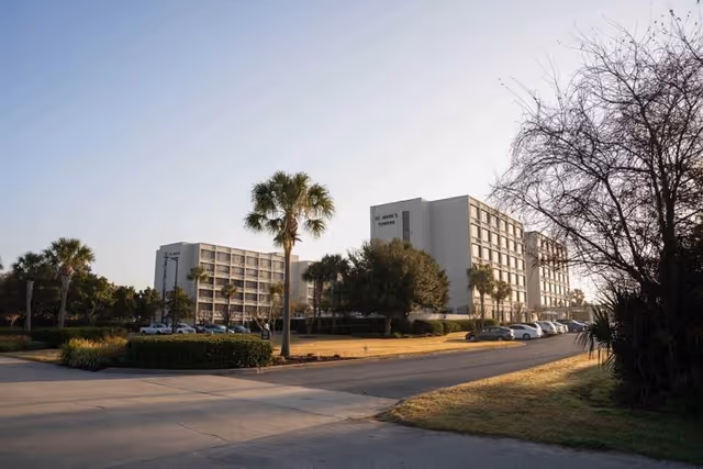 Exterior view of St Mark's Towers, a multi-story residential building surrounded by palm trees and parked cars under a clear sky during daylight.