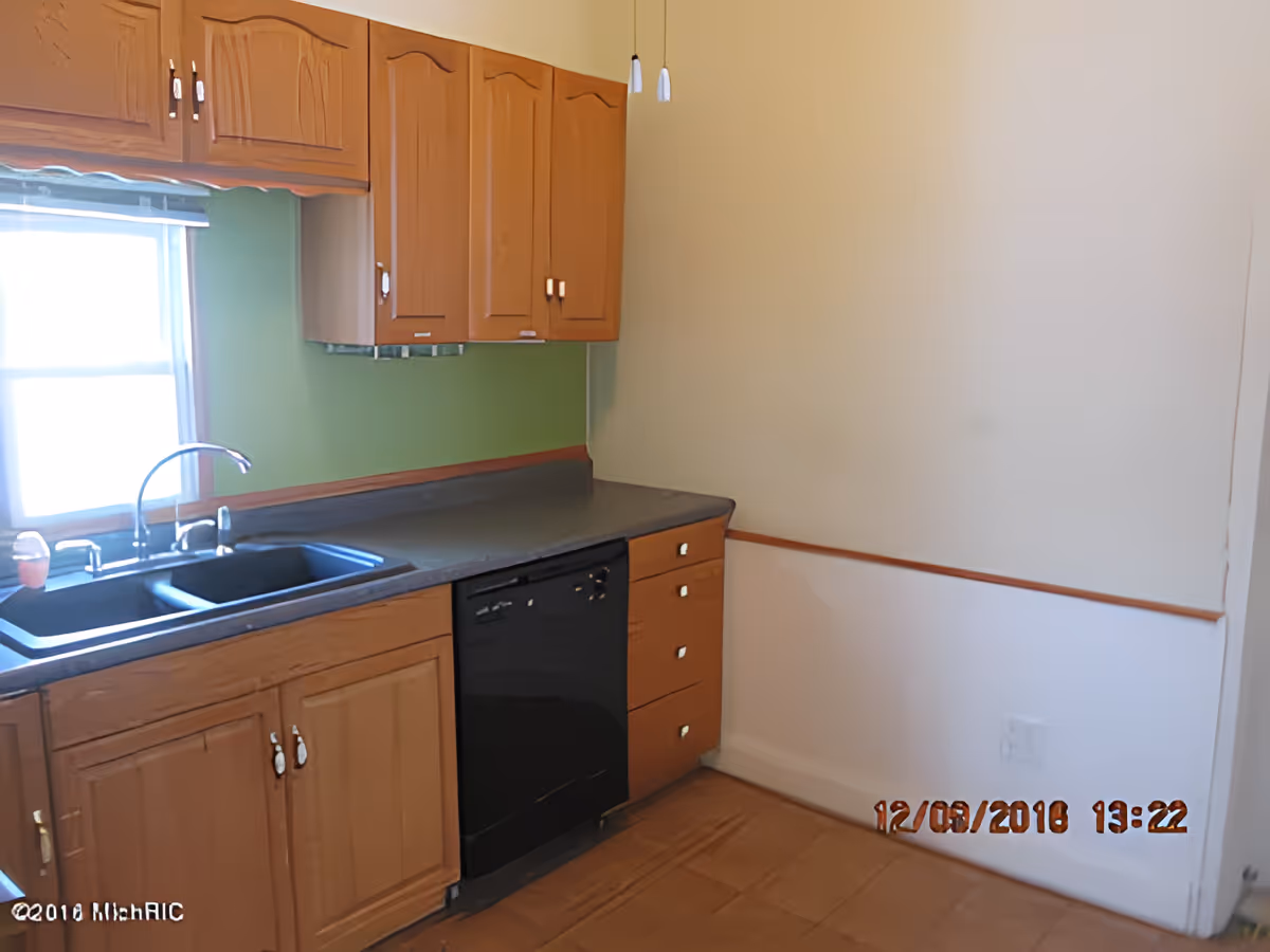 Kitchen with wooden cabinets, a double sink beneath a window, a dark countertop and a black dishwasher.