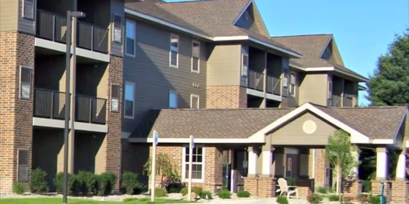 Exterior front of a multi-story senior living building with a covered entrance, balconies, and landscaped grounds.