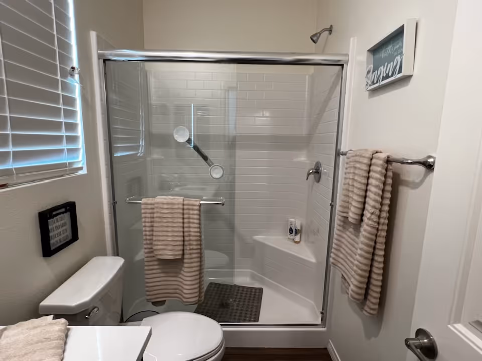 Small bathroom with a glass-enclosed shower, toilet, and beige striped towels hanging on racks.