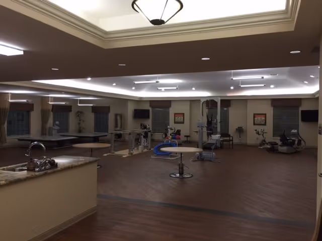 Spacious indoor rehabilitation/therapy room with exercise equipment, treatment tables, and a small counter with a sink in the foreground.