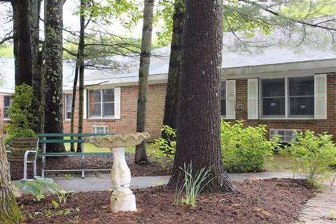 Outdoor garden area in front of a brick building with a bench and birdbath.