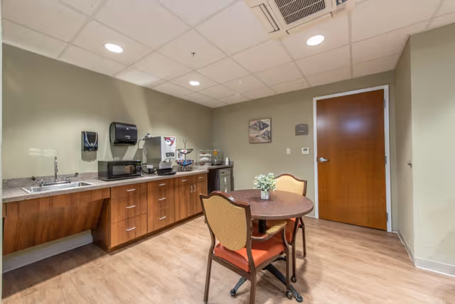 Small kitchenette and dining area with a round table and two chairs, a countertop with sink, microwave, and beverage station.