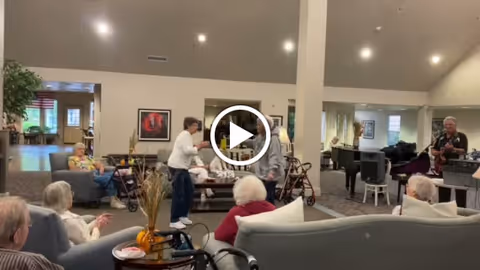 Community lounge with seniors seated on sofas and staff interacting during an activity.