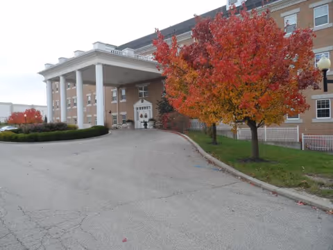 Exterior view of Laurelwood Assisted Living building with a covered entrance and fall trees.