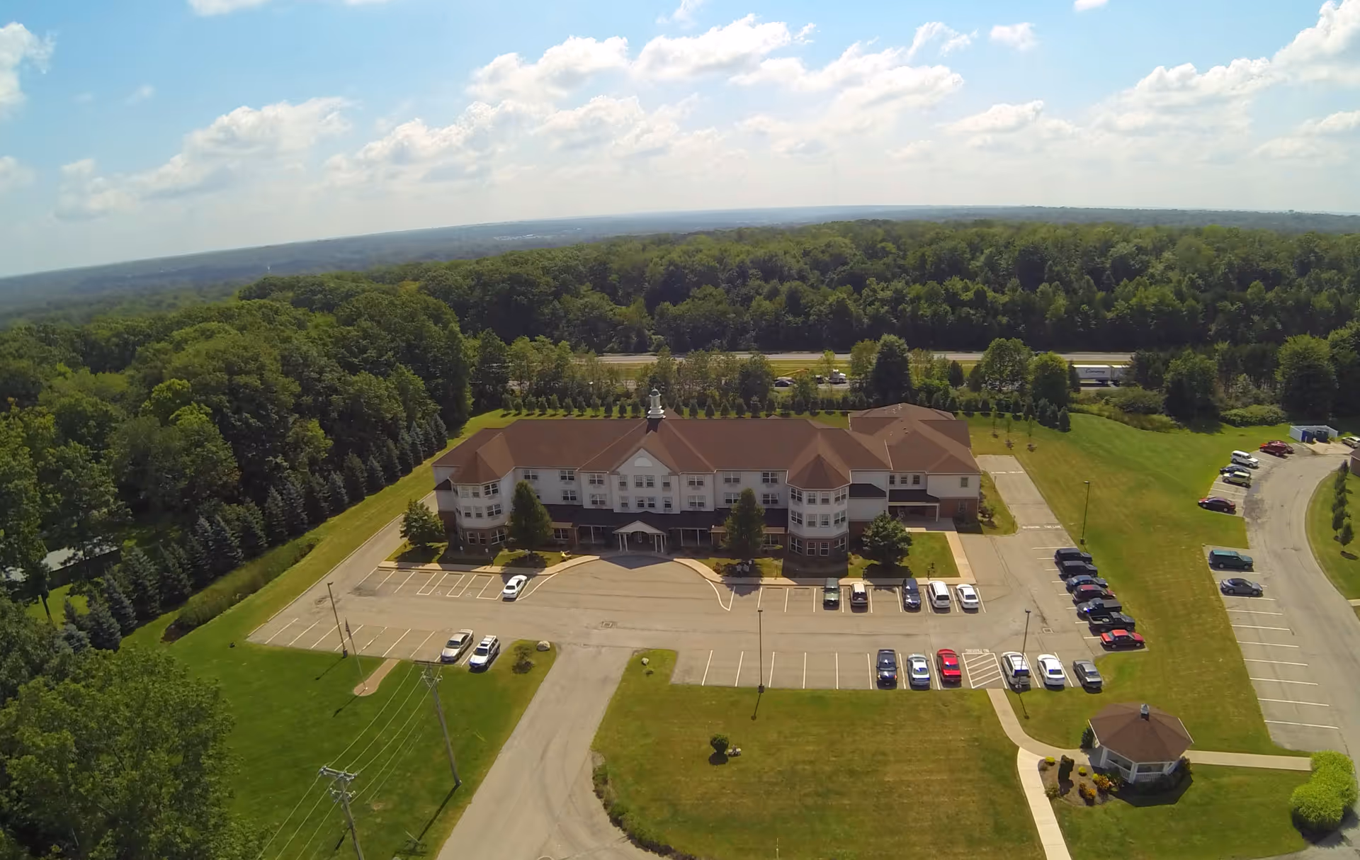 Aerial view of Liberty Arms Assisted Living exterior with parking lot and surrounding trees.