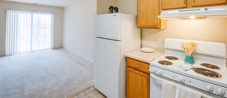 Open kitchen and living space with refrigerator, stove, wooden cabinets, and sliding glass door.