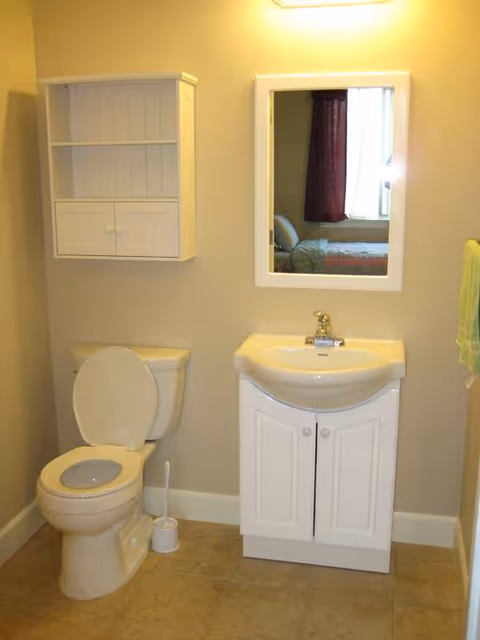 A clean bathroom with toilet, sink, mirror, cabinet, and towel.