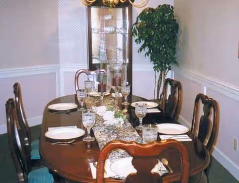 A formal dining room with a long table set for six in a senior living facility.