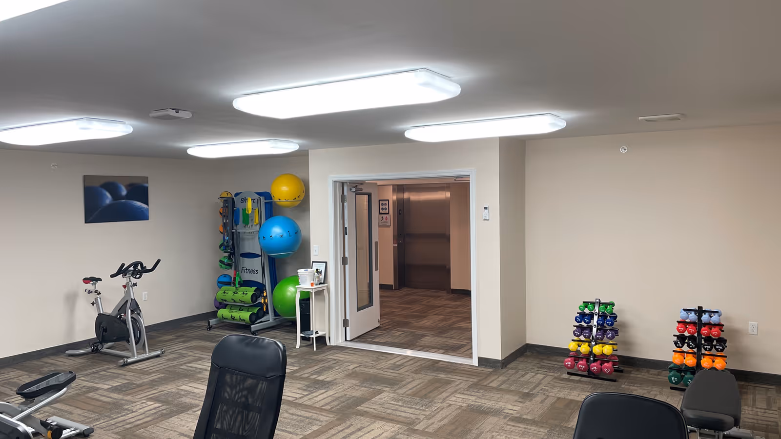 Bright, well-lit fitness room with an exercise bike, weight racks, stability balls and other workout equipment.