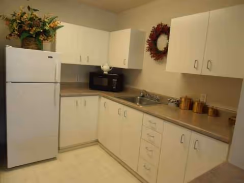 White kitchen with cabinets, fridge, microwave, sink, and decorative wreath.