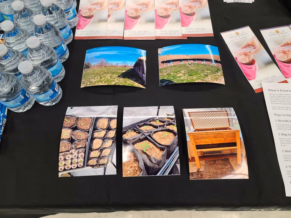 A table display with bottled water, brochures and printed photos showing outdoor shots and seedling plant trays.
