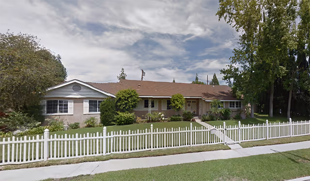 Single-story care home exterior with a white picket fence and landscaped front yard.