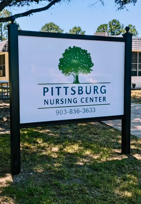 Outdoor sign reading "Pittsburg Nursing Center" with a green tree logo and phone number in front of the building.