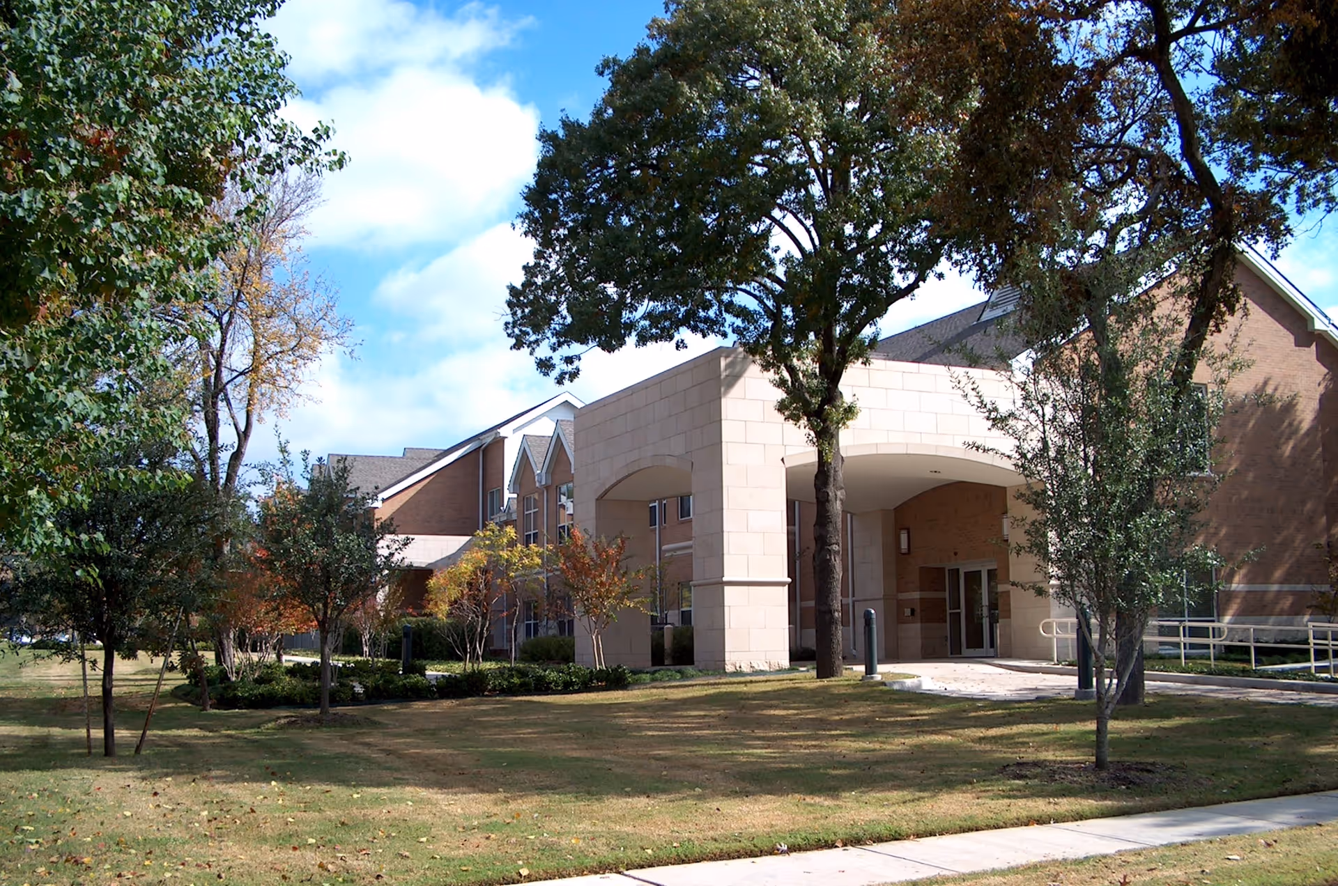 Brick senior living facility exterior with a covered entrance and surrounding trees.